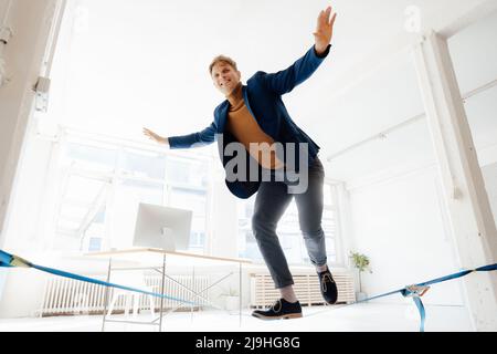 Glücklicher Geschäftsmann, der im Büro auf Gratwanderung ausbalanciert Stockfoto