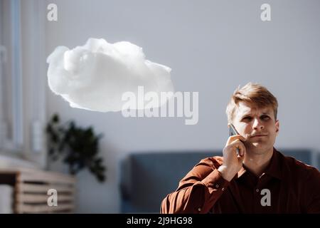 Ein Geschäftsmann, der auf einem Mobiltelefon sitzt, indem er im Büro ein Cloud-Netzwerk schweben kann Stockfoto