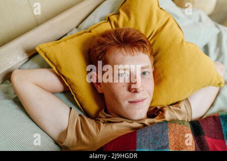 Lächelnder, rothaariger Teenager, der auf dem Bett liegt Stockfoto