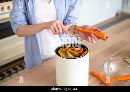 Frau schält zu Hause Karottenschälen im Kompostbehälter Stockfoto