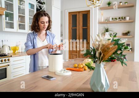 Junge Frau schält Karotten am Esstisch in der Küche Stockfoto