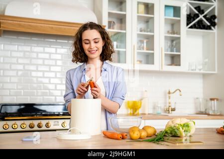 Lächelnde Frau, die Karotte am Esstisch in der Küche schälte Stockfoto