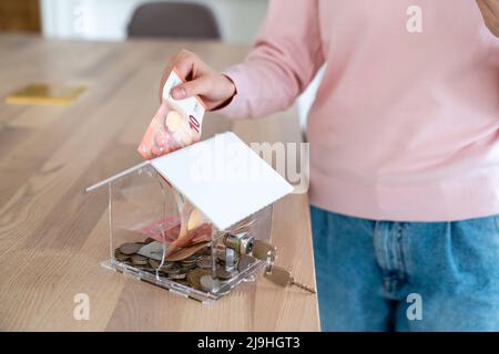 Frau, die zu Hause Papiergeld in Sparschwein legt Stockfoto