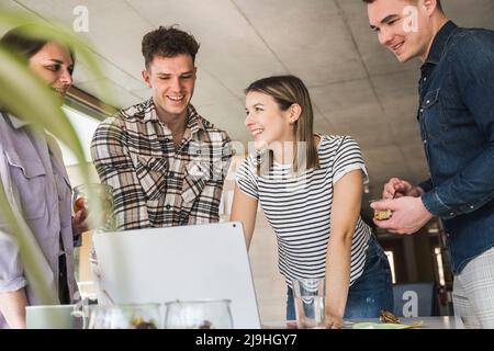 Junge Geschäftsleute, die sich im Büro einen Laptop teilen Stockfoto