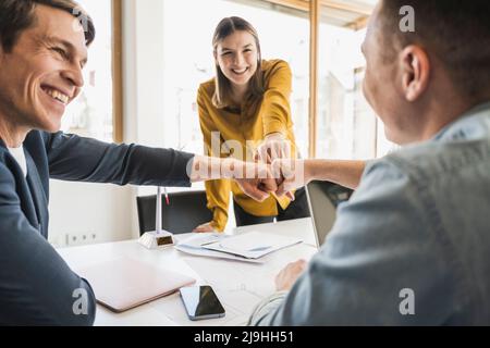 Glückliches Geschäftsteam, das die Fäuste im Büro anfasst Stockfoto