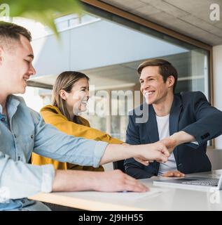 Glückliches Geschäftsteam, das die Fäuste im Büro anfasst Stockfoto