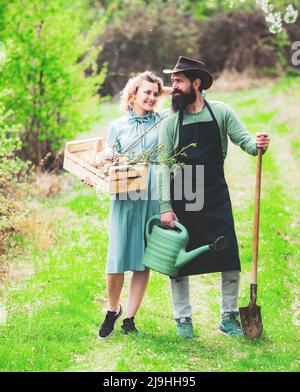 Frau und Mann verbringen Zeit im Obstgarten. Ein Paar Farmen trägt Kisten mit Gemüse und Gemüse entlang des Feldes. Stockfoto