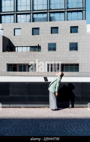 Geschäftsfrau, die sich vor dem Bürogebäude nach hinten beugt Stockfoto