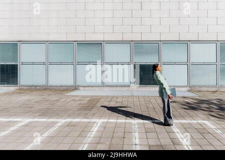 Junge Geschäftsfrau mit dem Laptop, der sich auf dem Fußweg nach hinten beugt Stockfoto