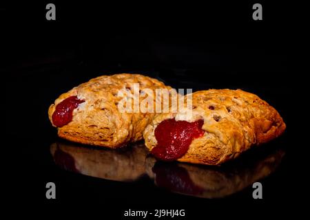 Zwei gebackene hausgemachte Brötchen mit roter Erdbeermarmelade, schwarzer Hintergrund Stockfoto