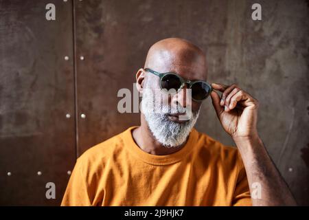 Kahler Mann mit Sonnenbrille, der vor der Wand steht Stockfoto