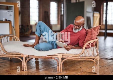 Glatter Mann mit Brille und Tablet-PC auf dem Sofa zu Hause Stockfoto