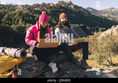 Junge Frau mit Laptop sitzend von Mann anpassen Sonnenkollektoren an sonnigen Tag Stockfoto