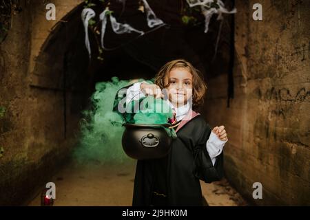 Nettes Mädchen hält Kessel mit Hexen brauen tragen Hexen Kostüm in gruseligen Tunnel Stockfoto