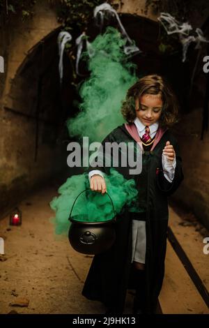 Lächelndes Mädchen trägt Kostüm hält Kessel mit Hexen brauen Stockfoto