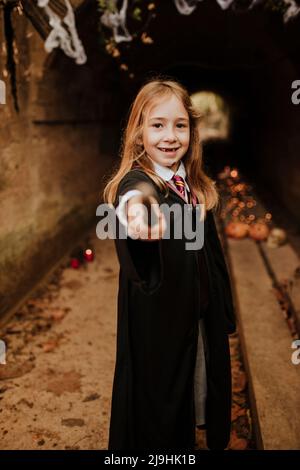 Lächelndes Mädchen mit Zauberstab, das Kostüm trägt und vor dem Tunnel steht Stockfoto