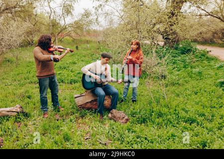 Mann übt Gitarre mit Freunden spielen Violine und Klarinette im Feld Stockfoto