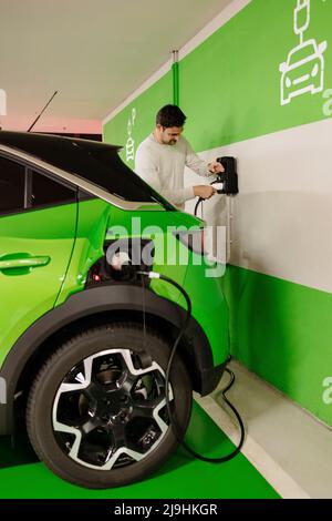 Mann, der Kabel einsteckt, um das Elektroauto an der Ladestation aufzuladen Stockfoto