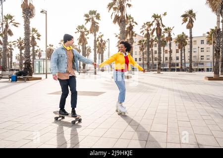 Glückliches Paar, das die Hände beim Schlittschuhlaufen auf dem Fußweg zusammenhält Stockfoto