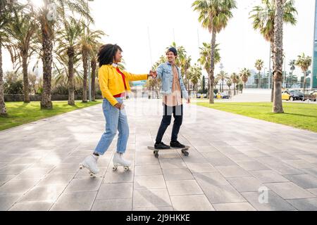 Glückliches Paar, das die Hände beim Schlittschuhlaufen auf dem Fußweg zusammenhält Stockfoto