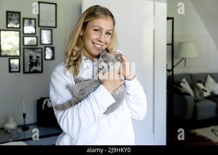 Lächelnde junge Frau mit grauer Katze zu Hause Stockfoto