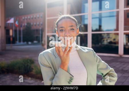 Lächelnde Geschäftsfrau, die an sonnigen Tagen Voicemail über das Mobiltelefon sendet Stockfoto