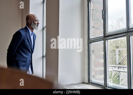 Nachdenklicher Geschäftsmann, der durch das Fenster zu Hause schaut Stockfoto