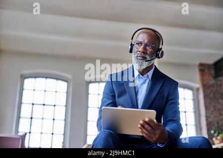 Durchdachter Geschäftsmann mit Headset, das den Tablet-Computer zu Hause hält Stockfoto