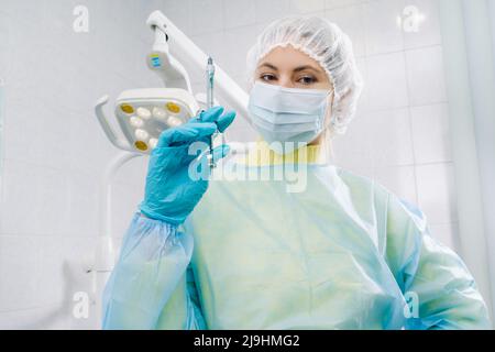 Ein maskierter Zahnarzt hält eine Injektionsspritze für einen Patienten im Büro. Stockfoto