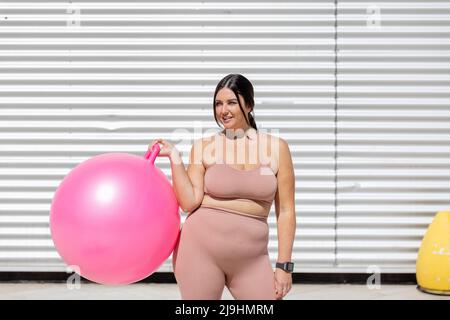 Kurvige Frau hält den Fitnessball vor der Wellwand Stockfoto