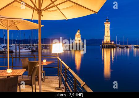 Deutschland, Bayern, Lindau, Langzeitbelichtung des beleuchteten Leuchtturms und der Bayerischen Löwenskulptur bei Nacht mit Restaurantterrasse im Vordergrund Stockfoto