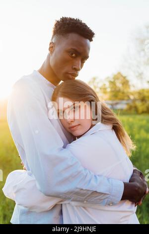 Multirassisches junges Paar, das sich an sonnigen Tagen in der Natur umarmt Stockfoto