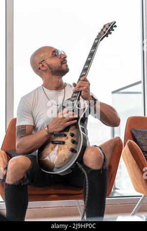 In einer luxuriösen Wohnung spielt ein junger kahler Mann seine E-Gitarre Stockfoto