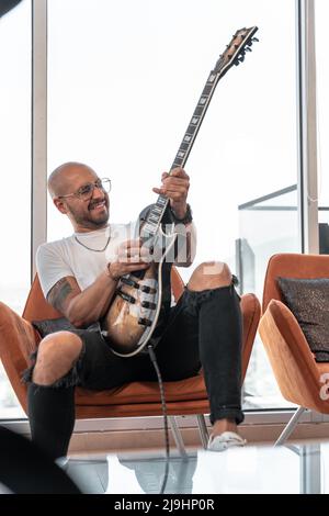 In einer luxuriösen Wohnung spielt ein junger kahler Mann aufgeregt seine E-Gitarre Stockfoto