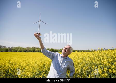 Lächelnder Mann, der das Modell der Windenergieanlage im Feld sieht Stockfoto