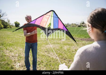 Lächelnder Großvater unterrichtet Enkelin am sonnigen Tag mit Drachen Stockfoto