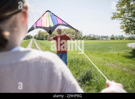 Glücklicher Großvater lehrt Enkelin fliegenden Drachen auf dem Feld Stockfoto