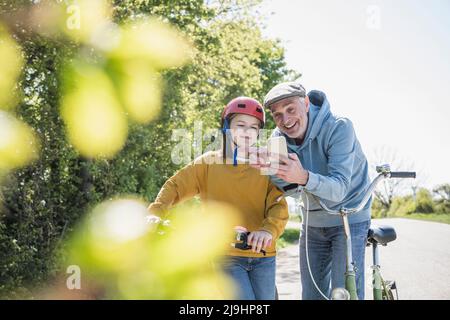 Glücklicher Großvater, der an einem sonnigen Tag mit seiner Enkelin ein Mobiltelefon teilt Stockfoto