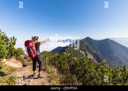 Deutschland, Bayern, Wanderin, die auf dem Gipfel des Heimgarten steht und auf Herzogstand zeigt Stockfoto