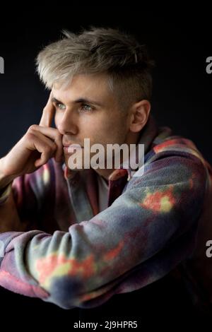 Nachdenklicher junger Mann vor schwarzem Hintergrund Stockfoto