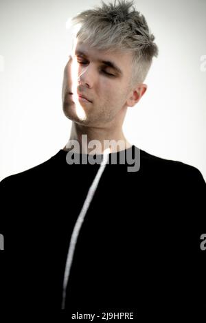 Junger Mann mit einem Lichtstrahl auf dem Gesicht, der vor weißem Hintergrund steht Stockfoto