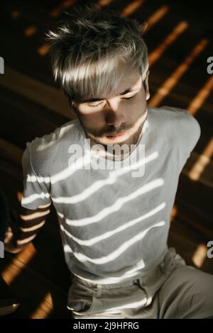 Junger Mann, der Sonnenlicht genießt und auf dem Boden sitzt Stockfoto