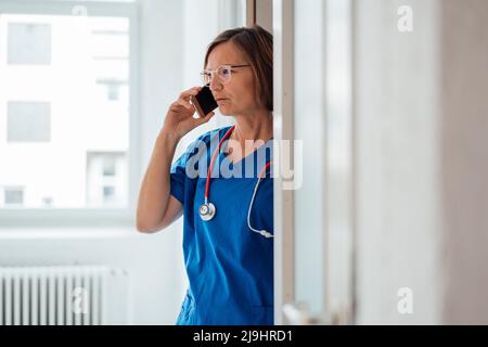 Arzt, der auf dem Smartphone spricht und in der Klinik vor der Tür steht Stockfoto