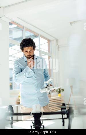 Ein nachdenklicher Geschäftsmann mit Fernbedienung und Blick auf die Drohne im Büro Stockfoto