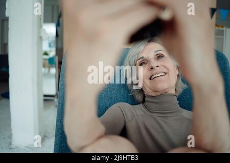 Lächelnde ältere Frau, die auf einem Stuhl sitzt Stockfoto