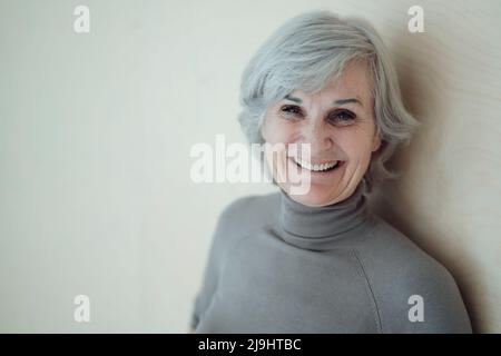 Glückliche ältere Frau, die vor der Wand steht Stockfoto