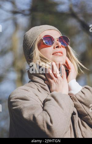 Blonde Frau mit Strickmütze und Sonnenbrille an sonnigen Tagen Stockfoto