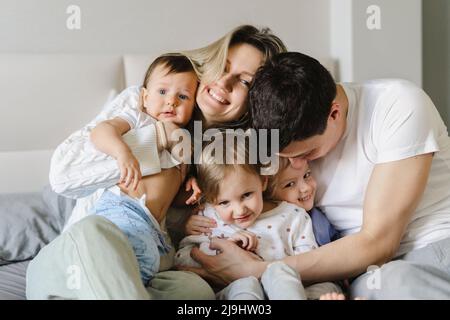 Eltern umarmen Kinder, die zu Hause auf dem Bett sitzen Stockfoto