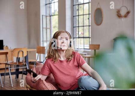 Frau mit Headset sitzt im Wohnzimmer zu Hause Stockfoto