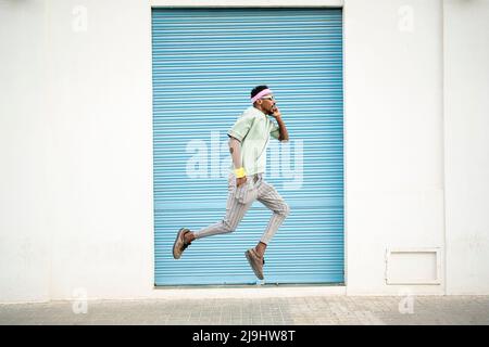Junger Mann mit der Hand in der Tasche springt mitten in der Luft auf dem Fußweg Stockfoto